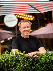 Matt McConnell standing behind a planter box and in front of red and white umbrellas at Bar Lourinhã.