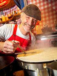 Michael Gatta-Castel wearing a beret and red apron, preparing a crepe at La Petite Crêperie.
