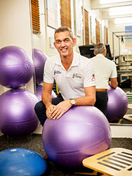 Michael Vadiveloo surrounded by exercise balls and other sports equipment in his clinic.