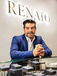 Renato Sassano in his store, leaning on a glass cabinet displaying fine jewellery.