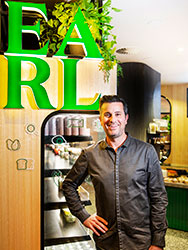 Simon O'Regan in front of large green 'EARL' sign above a fridge filled with takeaway food items.