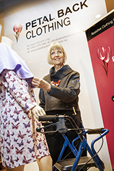 Smiling woman adjusting clothing on mannequin behind assistive chair walker