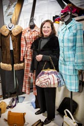 Eileen Carney standing beside three mannequins displaying tartan outfits and a fur coat. 