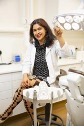 Leila Zamani sitting in a dental surgery holding the overhead light toward the camera.