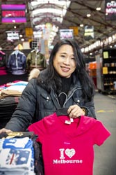Lisa Hong standing next to her stall at the Queen Victoria Market holding a t-shirt that reads ‘I love Melbourne’.