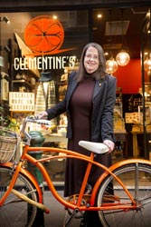 Melanie Ashe standing in front of a shop window with the sign ‘Clementine’s’, holding a vintage orange bicycle. 