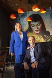 Stewart Koziora and Anna Carosa inside Asian Beer Café, standing in front of a wall painted with a large mural of a woman’s head. 