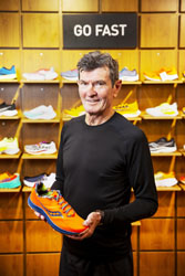 Terry O’Halloran holding a single runnign shoe while standing in front of a display of running shoes. A sign on the wall reads ‘go fast’.
