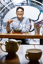 Smiling man eating from bowl with chopsticks