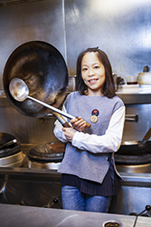 Smiling woman in kitchen holding a wok and ladle