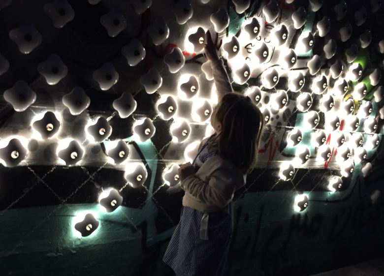 A girl touches lights arranged in a display on a brick wall.