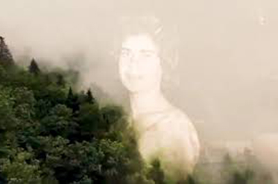 Human figure superimposed in sky next to tree-covered hills 