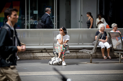 Woman sitting on city street bench wearing headphones