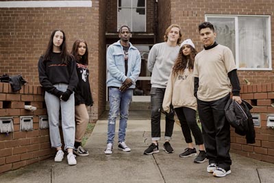 Young people standing at the entrance to a block of flats, wearing HoMie clothing