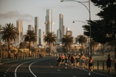 A group of cyclists riding along a road with the Melbourne skyline in the background