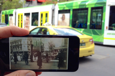 Hand holding phone up on street, with screen showing same location in past