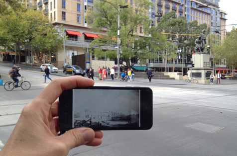Hand holding phone up on street, with screen showing same location in past