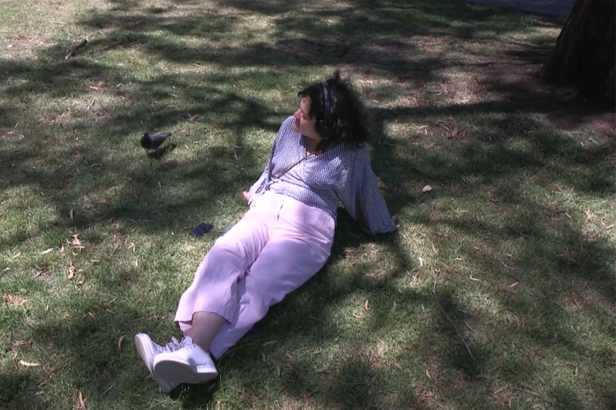 A photograph of a person sitting down under a tree while wearing over-ear headphones.
