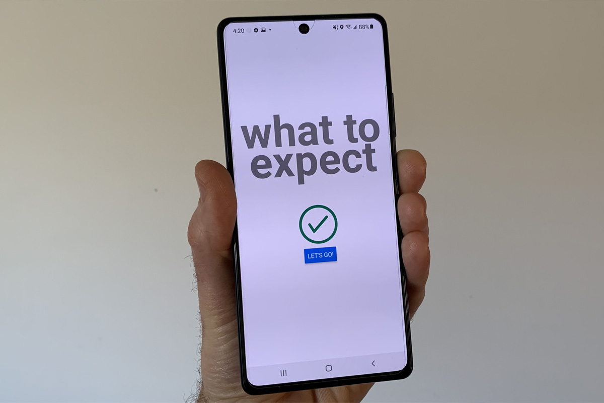 A photograph of a person's hand holding onto a smart phone with an app open called 'What to Expect'.