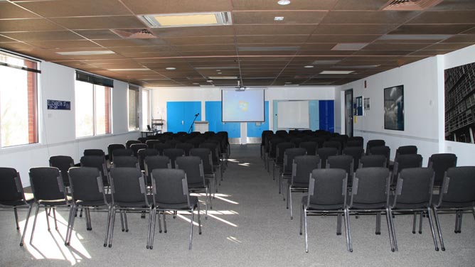 A large room with chairs set in rows facing a projected screen and lectern