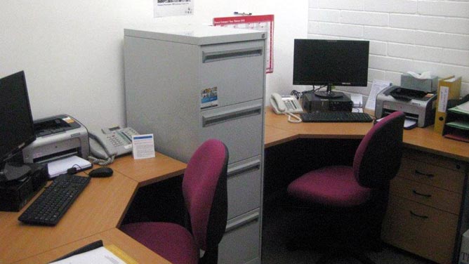 Two corner desks with computers, printers and other office equipment in a small room
