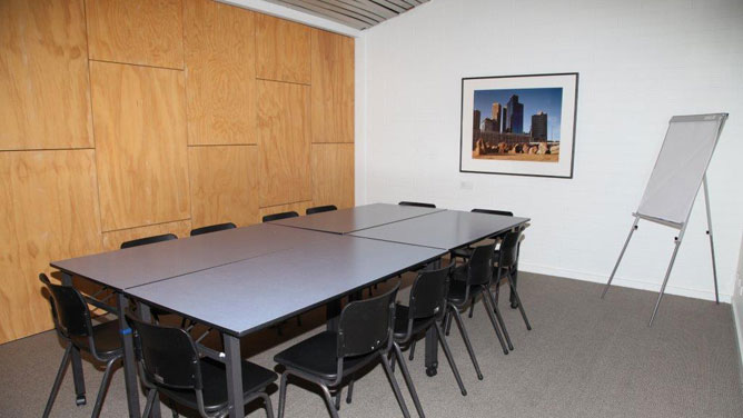 A room with timber wall, whiteboard, 12 chairs around four small tables grouped as one