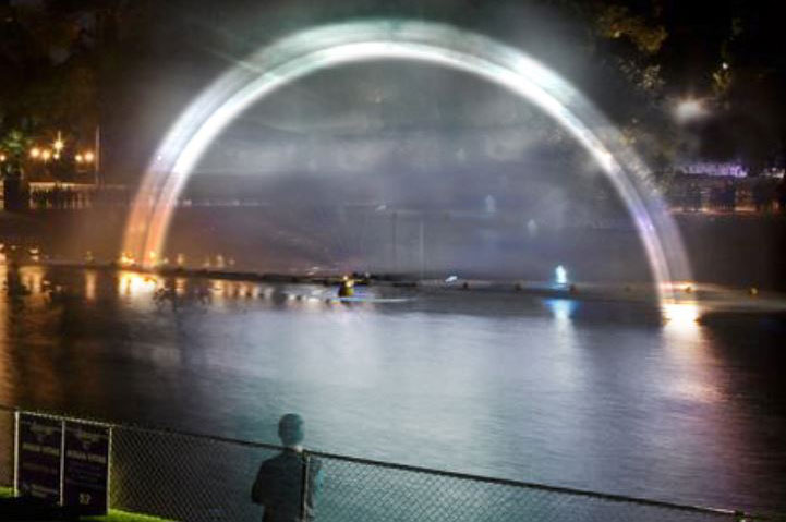 'Monotone rainbow' artwork on the river at night. A person is seen in the foreground looking towards the rainbow.