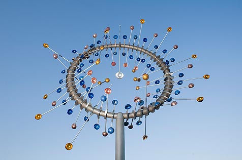 Metal sculpture of a pole with hoop attached which has radiating armature and cups on a pole