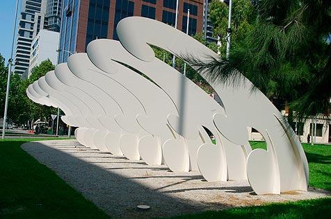 Sculpture of flat wave-like forms lined up in a row, in city park setting
