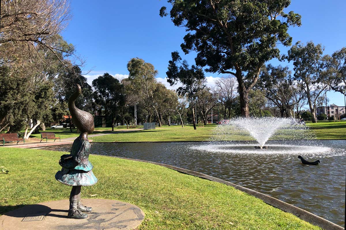 Bronze scuplture of a young girl standing and facing the pond, with her long hair sticking up playfully.