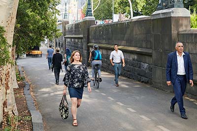 People walking and cycling along a wide shady path in the city