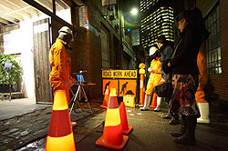 Art installation in laneway with person in protective gear standing in area cordoned off by traffic cones and 