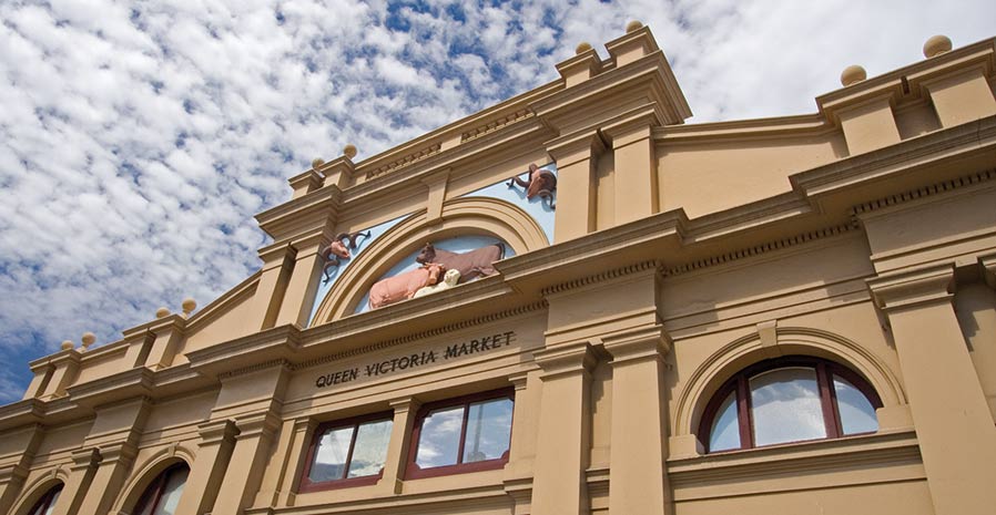 Exterior of Queen Victoria Market building showing architectural details, yellow facade and embossed images of livestock above the entrance sign.