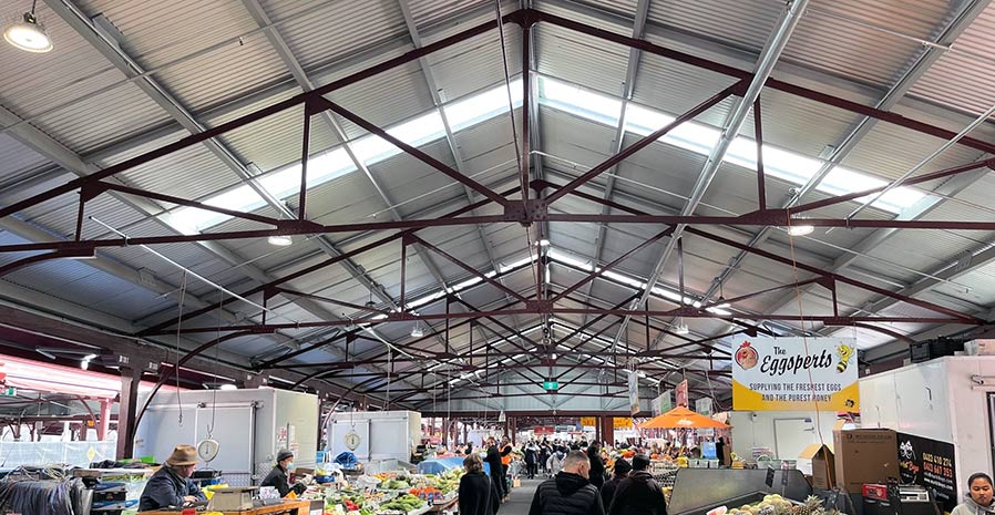 Looking up to the ceiling and roof of the market shed, showing its wide metal trusses and corrugated iron roofing