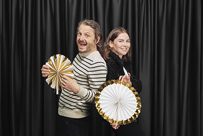 Two people standing back to back holding party decorations and smiling. 