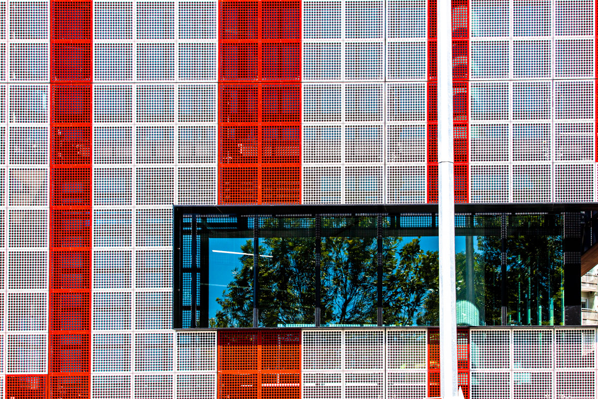 Detail view of one side of a building clad in red and white metal screens.