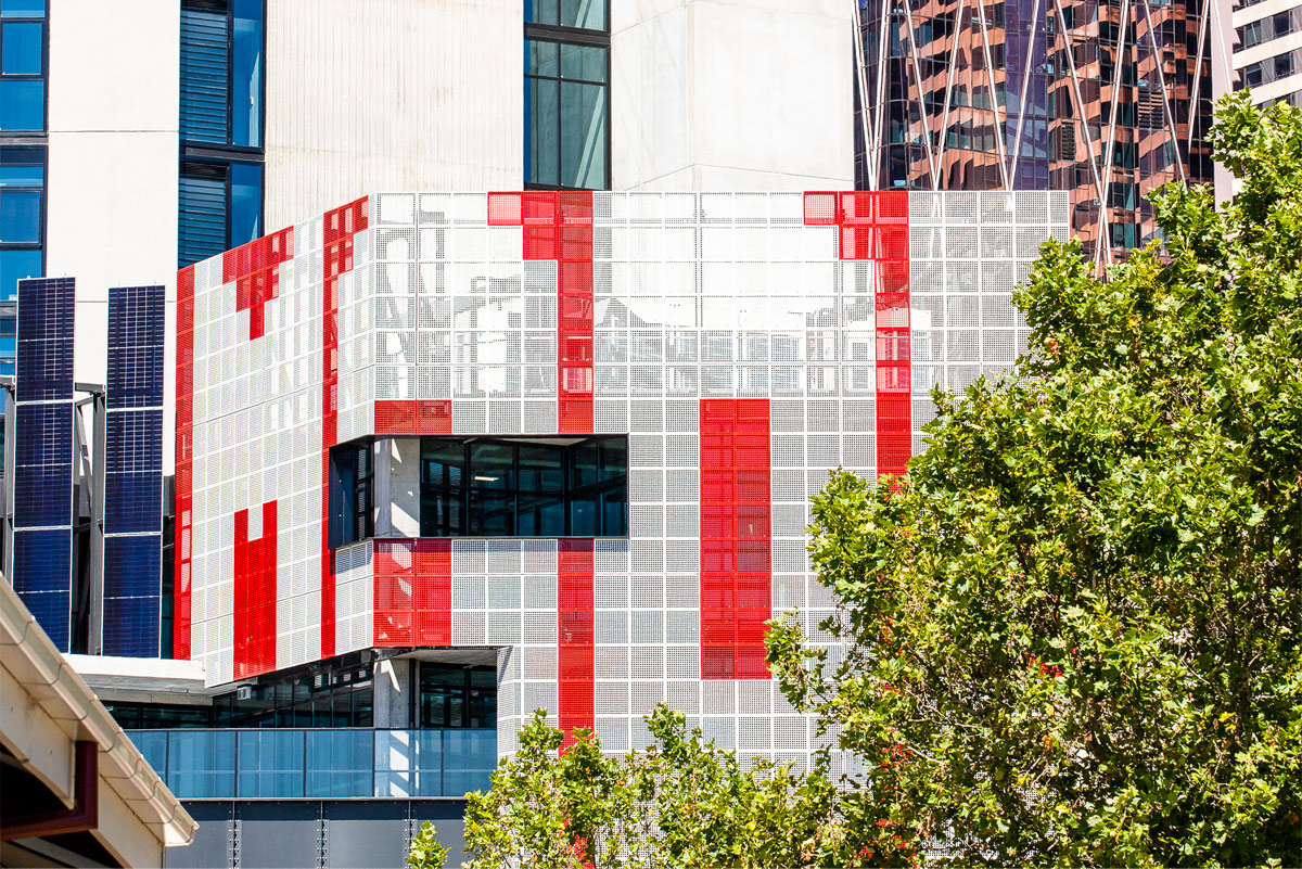 View of the red and white perforated metal screens on top a building. Taller buildings in the background.