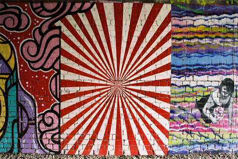Red and white starburst pattern painted on a brick wall and surrounded by other patterns.