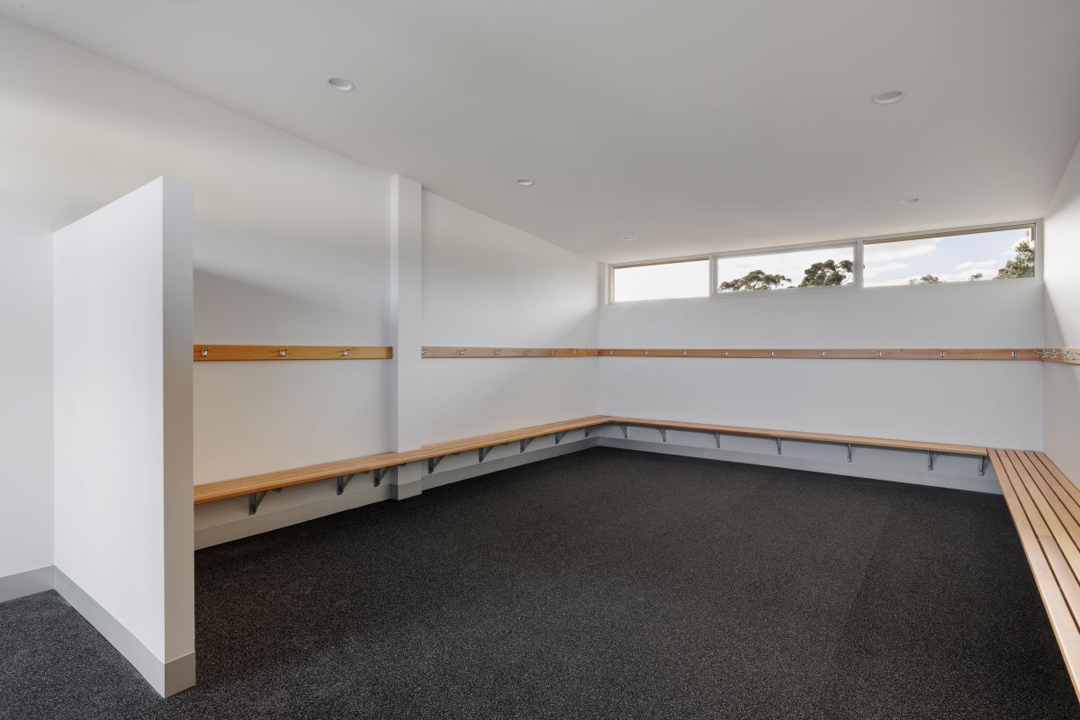 A change room with grey floor, wooden benches and white walls.