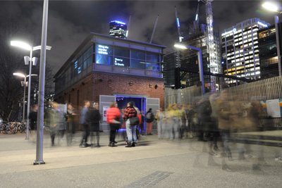 A brick building photographed at nighttime, with blurred silhouettes of people standing near the entrance