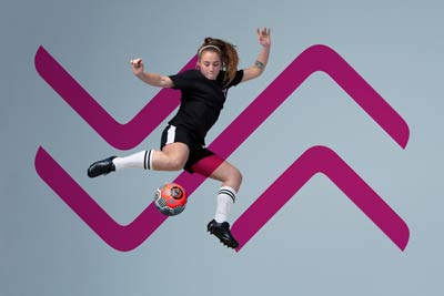 A woman dressed in sports gear, leaping in the air and about to kick a soccer ball