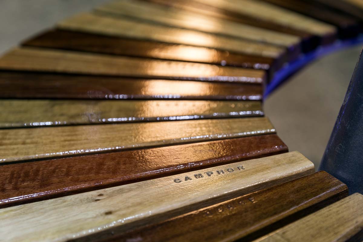 Close-up showing the bench's wooden slats in different shades of brown, labelled with the timber types including 'Camphor'