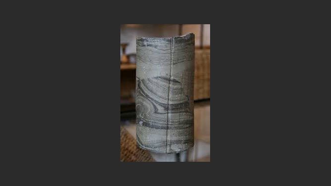 Cylindrical sculpture made of rock-like material with layers in varying shades of gray