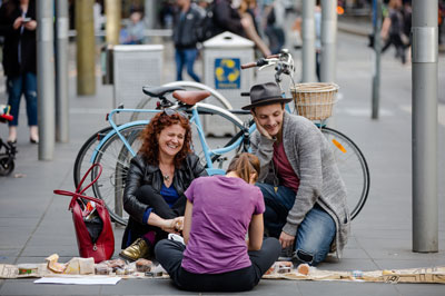 Woman sitting on ground creating artowrk with two other people sitting and watching