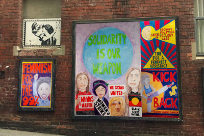 Colourful hand-drawn posters mounted on a wall, illustrated with feminist images and messages