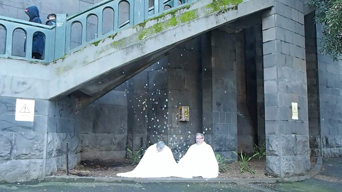 The artists sitting among floating bubbles amd underneath stairs leading to a bridge