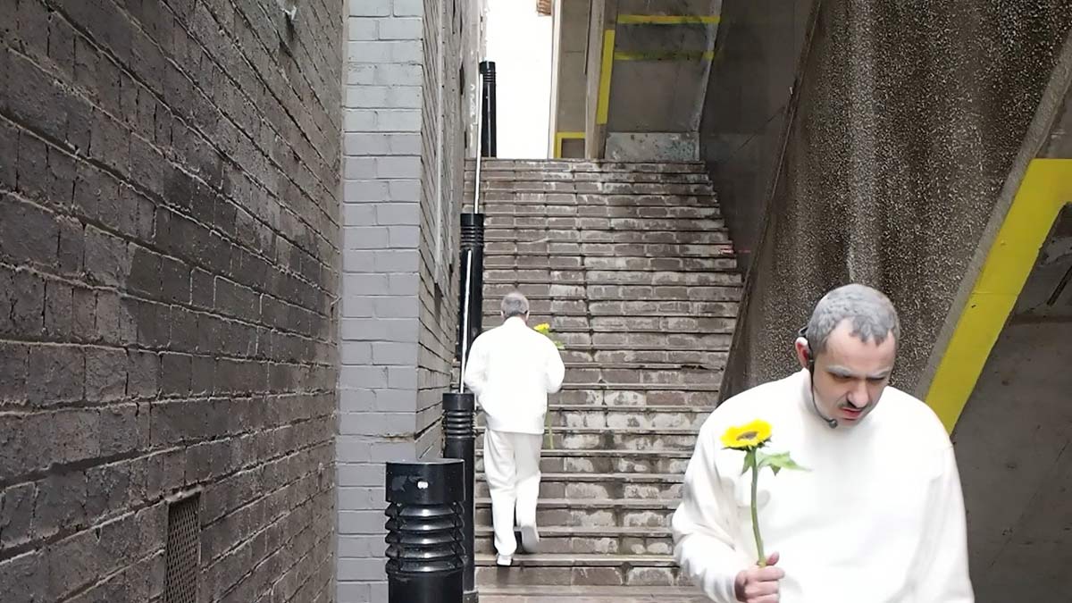 One artist walking up the stairs, the other facing away at the bottom. Both are holding a single sunflower.