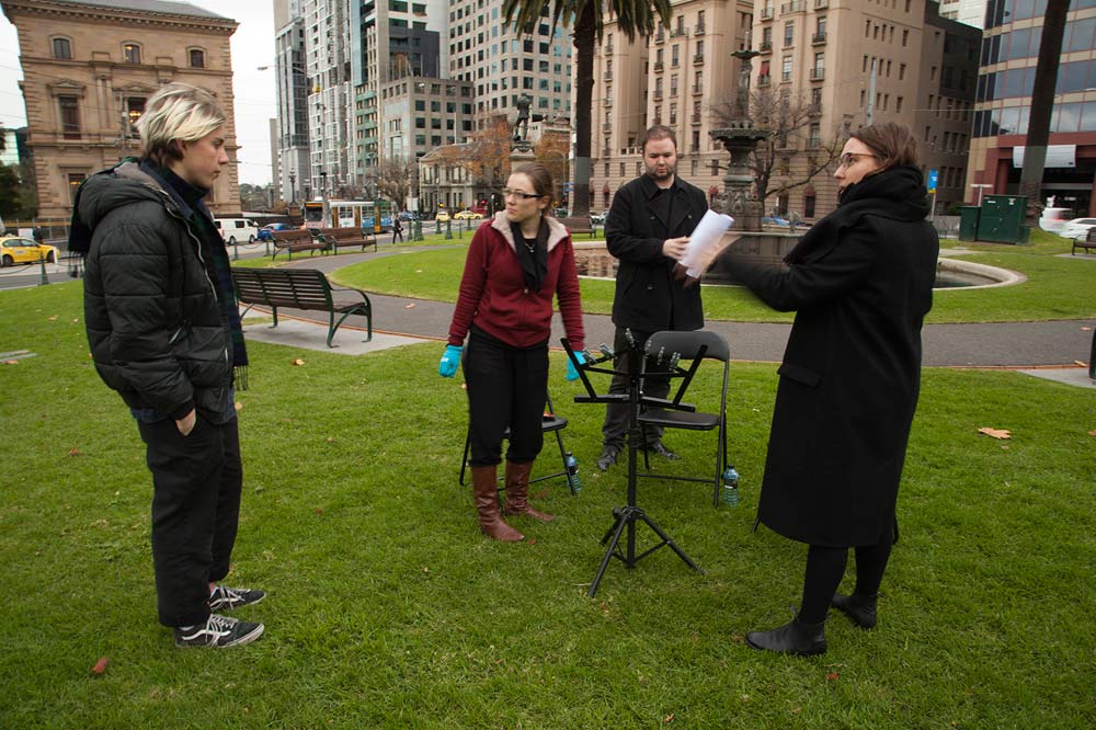 The artist and several musicians standing in public green space in the city with chairs and music stand set up