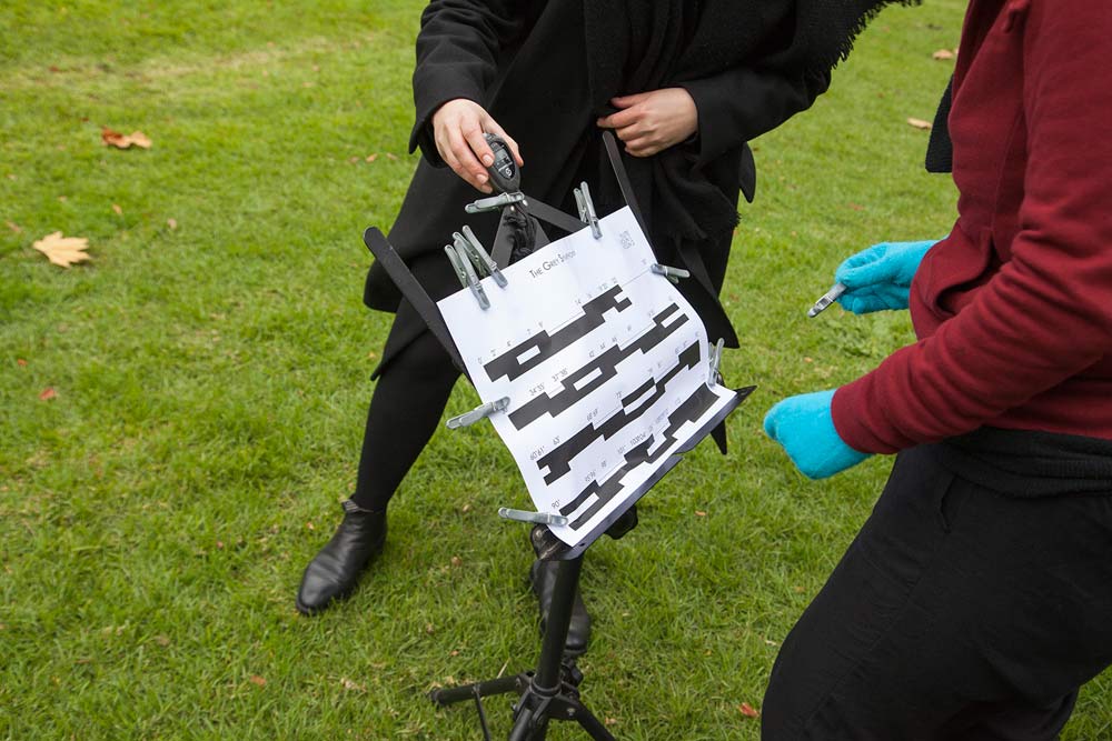 Two people attaching a music chart for 'The Grey Symphony' to a music stand with clothes pegs
