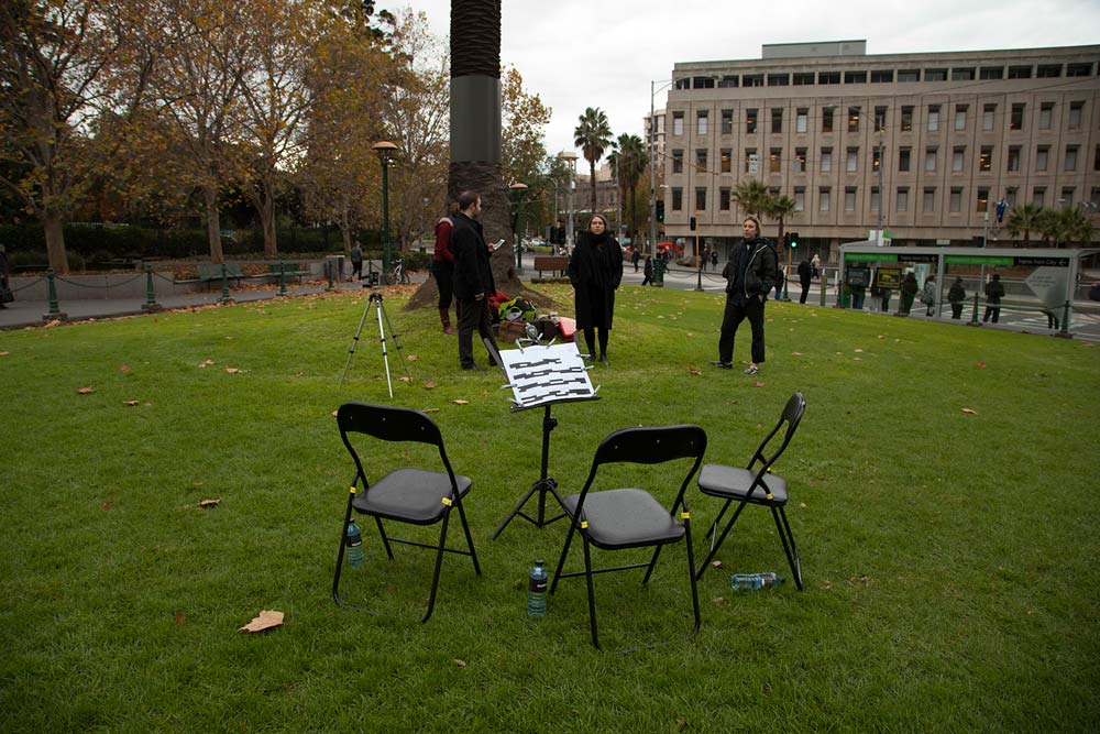Artist and several musicians standing near chairs and music stand set in public green space